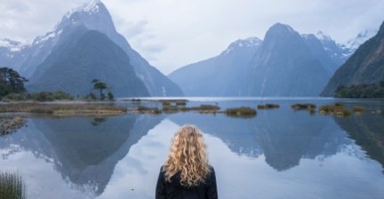 Person looking at the calm waters and dramatic peaks of Milford Sound