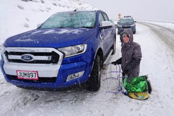 Person kneeling beside a blue Ford truck on a snowy road