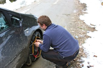 Man putting snow chains on a car tire on a snowy roadside