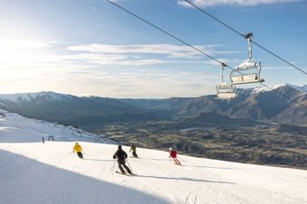 Skiers going downhill with a chairlift above and mountain views in the distance