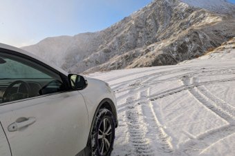 White SUV parked on a snow-covered mountain road with tire tracks visible