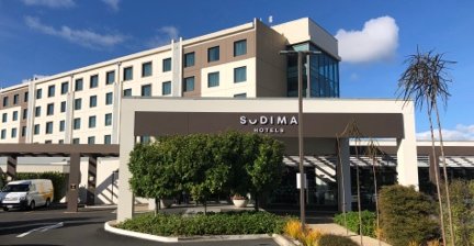 Exterior view of Sudima Auckland Airport hotel with trees and blue sky