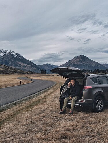Image of a couple sitting in the back of a GO Rentals Rav4 Rental Car with snow-capped mountains in the background