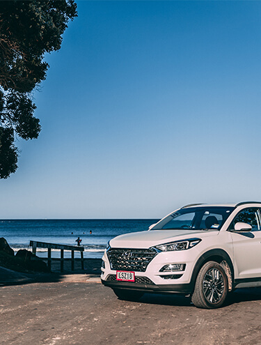Image of a white Hyundai Santa Fe parked next to the beach with GO Rentals pink licence plates