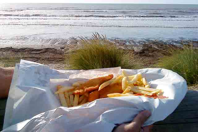 Image of fish and chips wrapped in newspaper with the beach and sea in the background