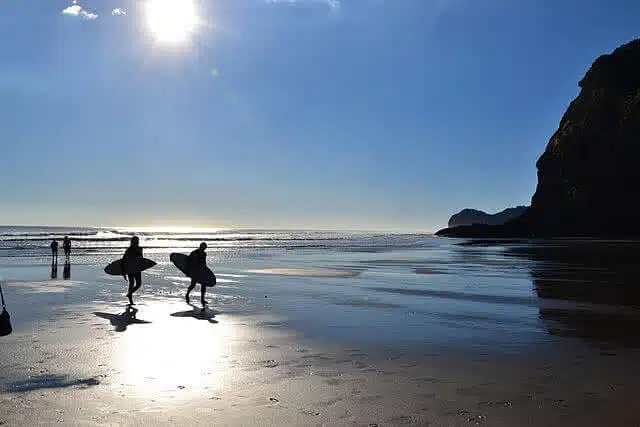 Surfers walking back up the beach at Piha, West of Auckland