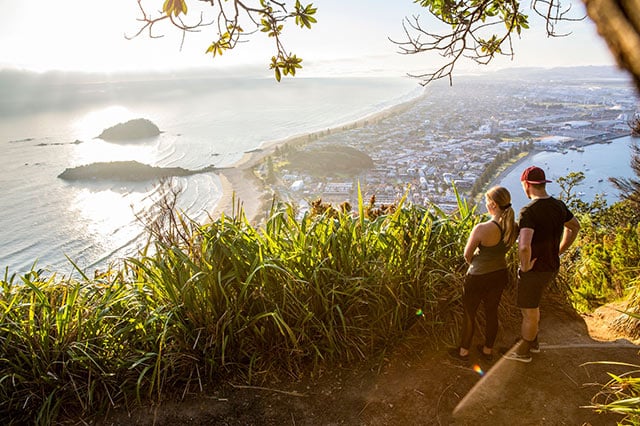 2 people standing at the top of a lookout looking out over a town and the ocean