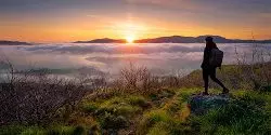 Mobile menu image of a male stood on a rock at the top of a mountain overlooking a landscape covered in cloud