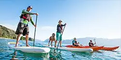 Two people on stand up paddleboards and two people in kayaks on the crystal clear water on a sunny day - mobile