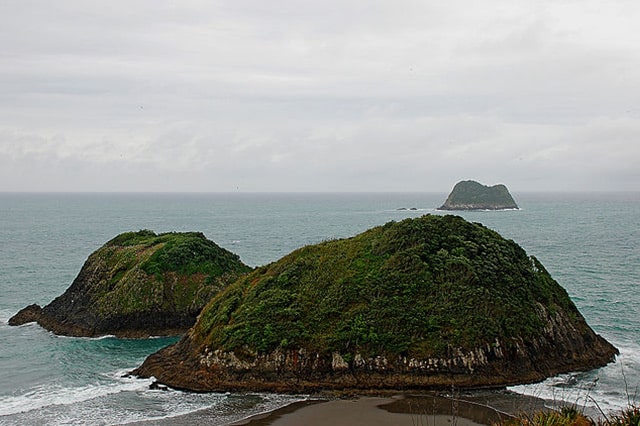 Two small, vegetation covered, dome shaped islands with a third in the distance/