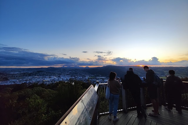 4 people standing at the Parihaka look out overlooking Whangarei at dusk.