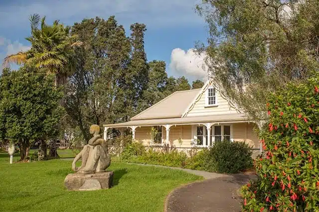 A stone statue os a man sitting on the lawn in front of the Victorian Era Reyburn House.