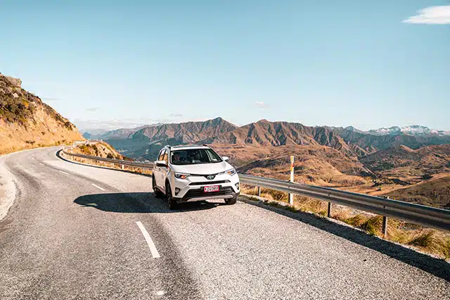 A white car driving with rolling hills and mountains in the background