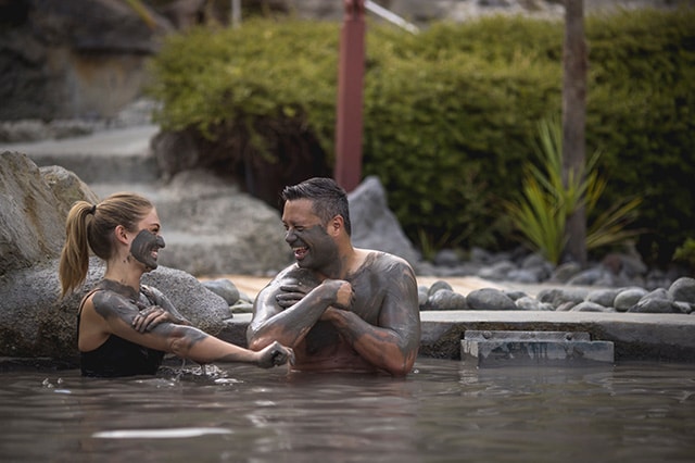 a couple laughing as they cover themselves in mud in the mud pools