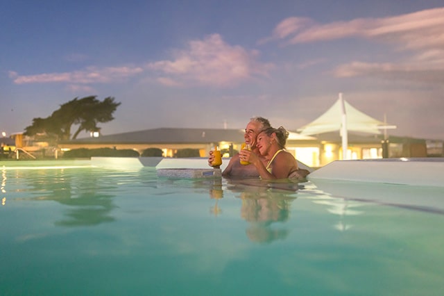 a couple sitting in a large hot tub drinking orange cocktails