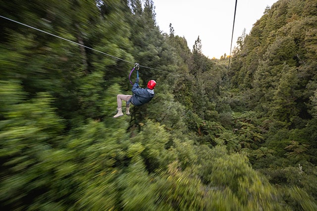 man in red helmet going down zipline above the forest