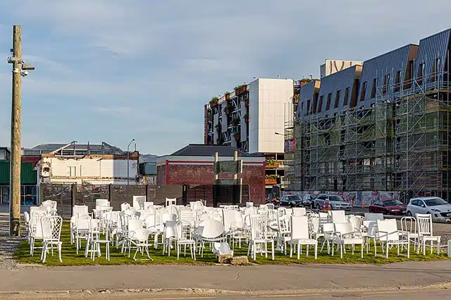 185 empty white chairs laid out on a patch of grass near the sidewalk
