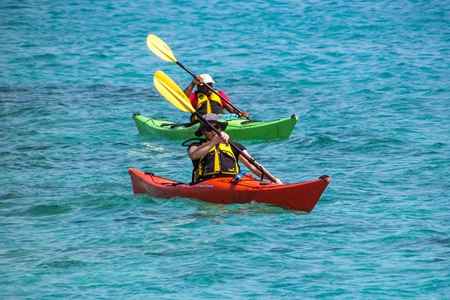 two people with yellow life jackets. One in a green kayak, the other in a red kayak