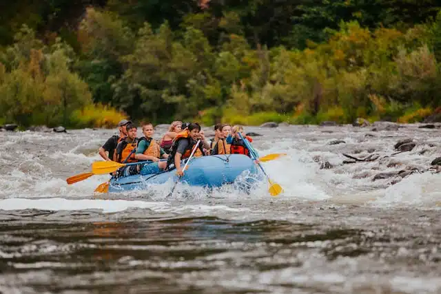a group of kids rowing a blur raft down some white water rapids