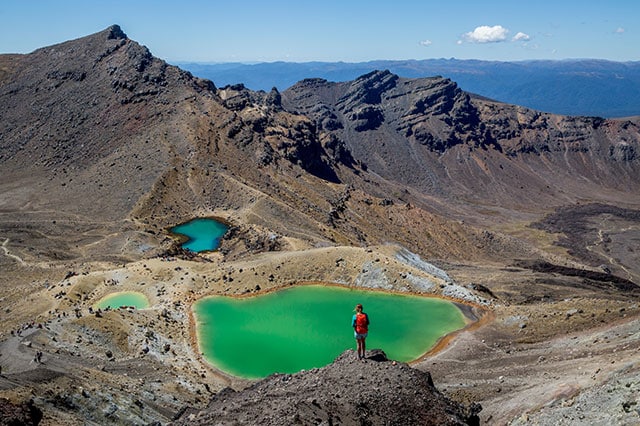 A person standing on a hill looking over the emerald green sulphur pool in the volcanic surroundings