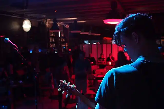 A man playing guitar in a dimly lit room performing to a small crowd