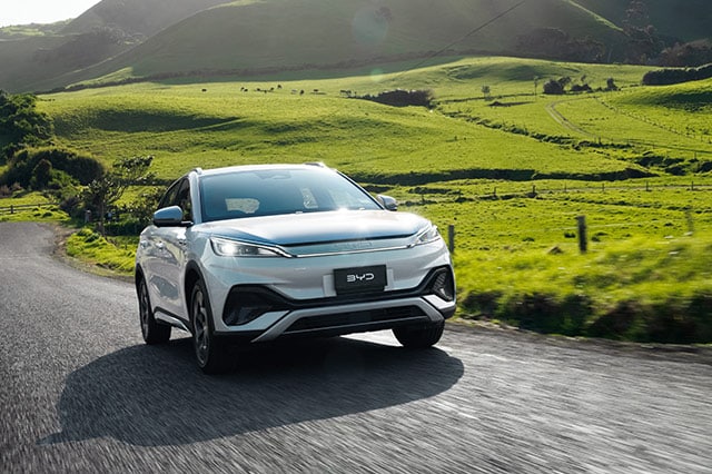 BYD Atto 3 vehicle driving on road with green grass and mountain background