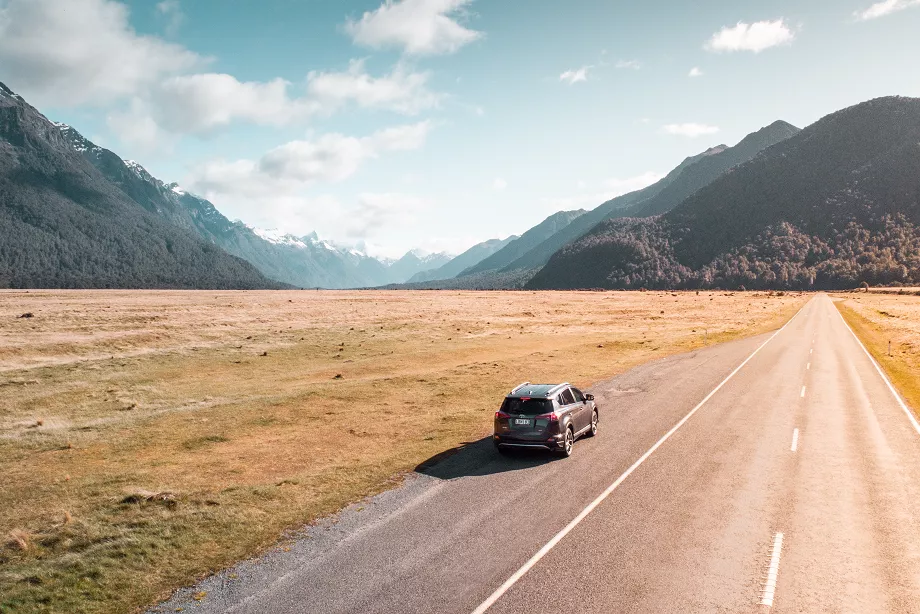 car parked on the left side of new zealand milford road with mountain landscape in background