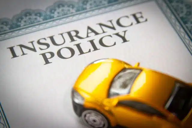 yellow toy car on top of insurance policy paperwork