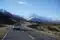 White car driving on left-hand side of the road in new zealand with mountain landscape background