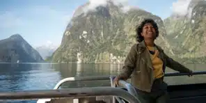 Smiling woman enjoying a scenic boat ride through a fjord surrounded by lush green mountains